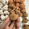 A hand holds a cluster of handcrafted crochet animal keychains in various shades of brown and cream.