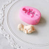 Pink silicone cake molds with measurements are displayed on a white plate next to a baby figurine.