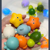 A hand holds multiple glow-in-the-dark animal washing water toys in various colors like yellow, orange, green, and blue.