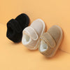 A pair of cozy leather winter boots for toddlers, shown in black and beige colors, resting on a light orange background.