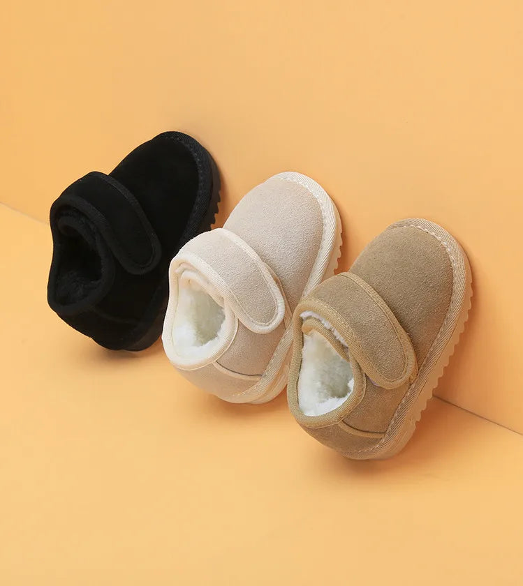 A pair of cozy leather winter boots for toddlers, shown in black and beige colors, resting on a light orange background.