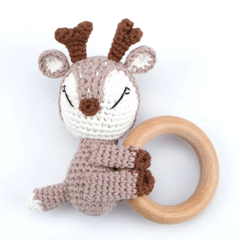 A crocheted animal toy resembling a deer or fawn with brown and white fur, attached to a wooden ring.