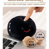 A close-up of a black plush doll with a smiling face being held by a hand, next to a laptop keyboard.