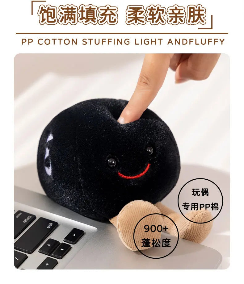 A close-up of a black plush doll with a smiling face being held by a hand, next to a laptop keyboard.