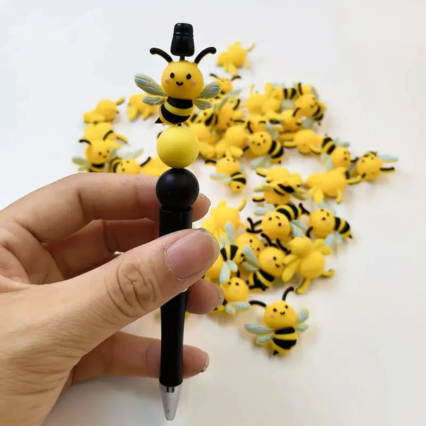 A hand holds a black silicone bead with a yellow bee charm, surrounded by many similar yellow bee beads for DIY crafts.