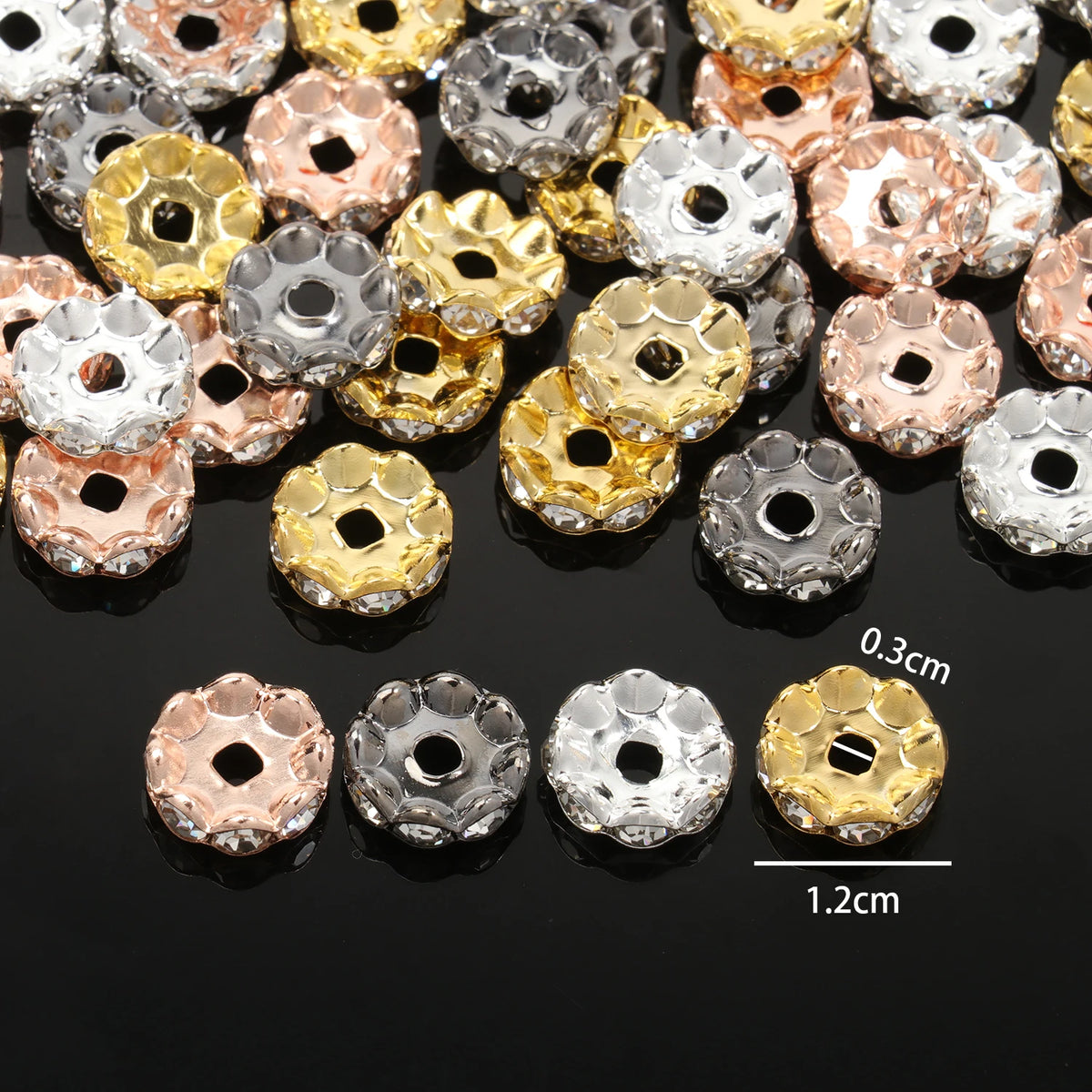 A collection of 12mm crystal rhinestone spacer beads in various gold and silver tones are displayed on a dark surface.