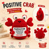 A red crochet crab toy with a motivational card, shown from multiple angles.