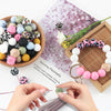Hands are assembling silicone beads for DIY jewelry making, surrounded by various colored and patterned beads.