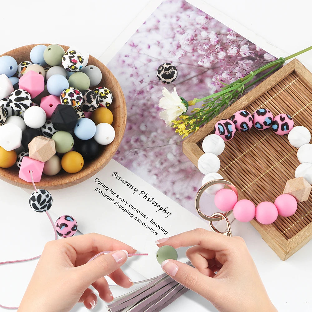 Hands are assembling silicone beads for DIY jewelry making, surrounded by various colored and patterned beads.