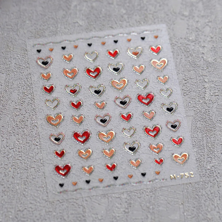 A sheet of nail art stickers featuring various heart shapes in red, pink, and gold tones on a gray background.