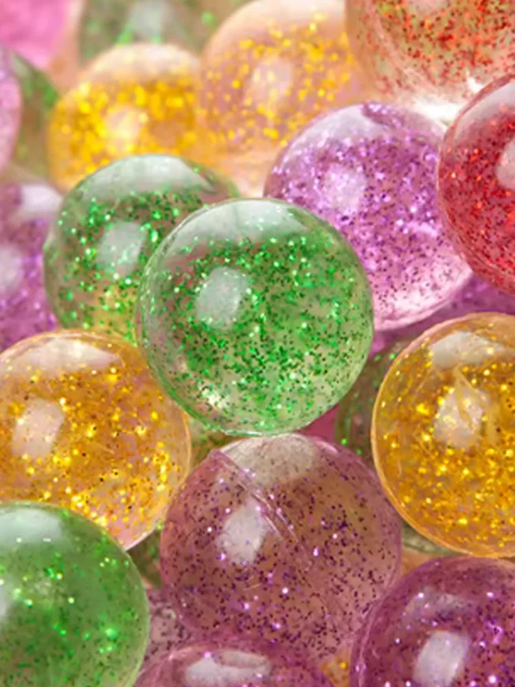 A close-up of various colorful glitter bouncy balls in shades of green, yellow, and purple.