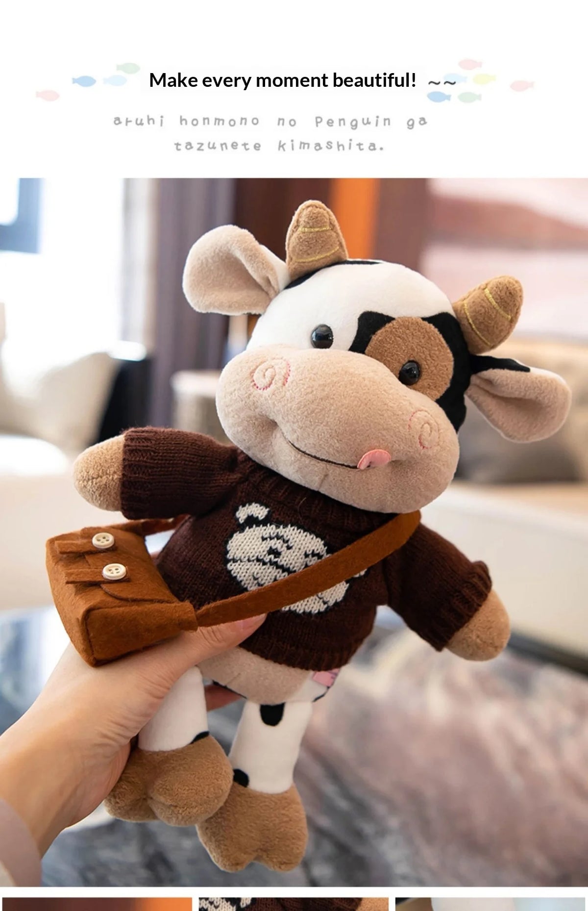 A hand holds a brown and white plush cow stuffed animal with a leather strap.