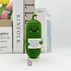 A handwoven green crochet pencil ornament with a pink flower detail sits in front of a stack of books.