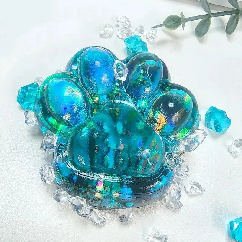 A vibrant blue and teal cat paw squishy fidget toy made of resin with clear crystals surrounding it.