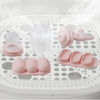 A silicone fruit food feeder and cooling mold set with various pink silicone shapes placed on a white grid tray.