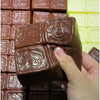 A hand holds a brown squishy toy shaped like a strawberry with embossed details against a background of similar toys.