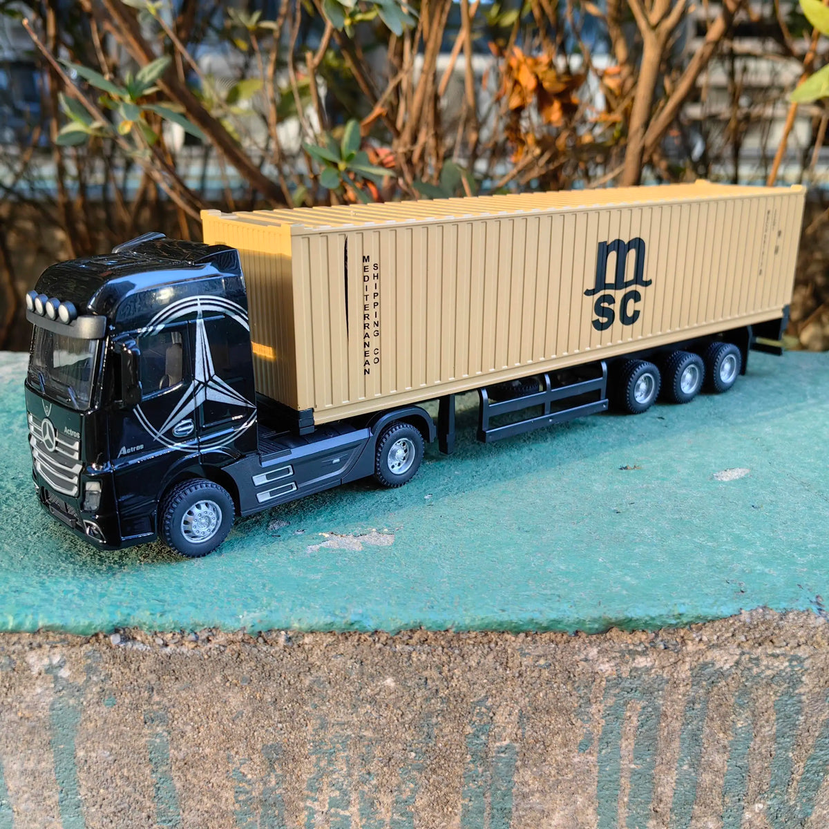 A black diecast container truck with a tan box and MSC logo parked on a green surface.