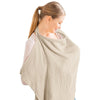 A woman wearing a beige breathable muslin nursing cover with an adjustable neckline.