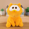 An orange Garfield plush doll with large eyes and black whiskers sitting on a wooden surface.