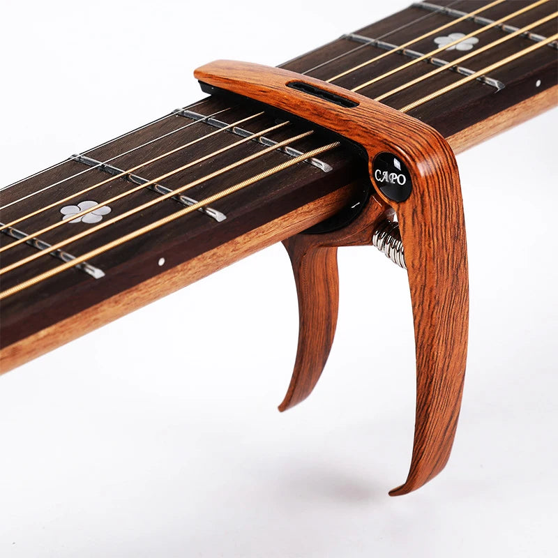 A close-up view of a wooden guitar fretboard with a metal capo and pick holder attached.