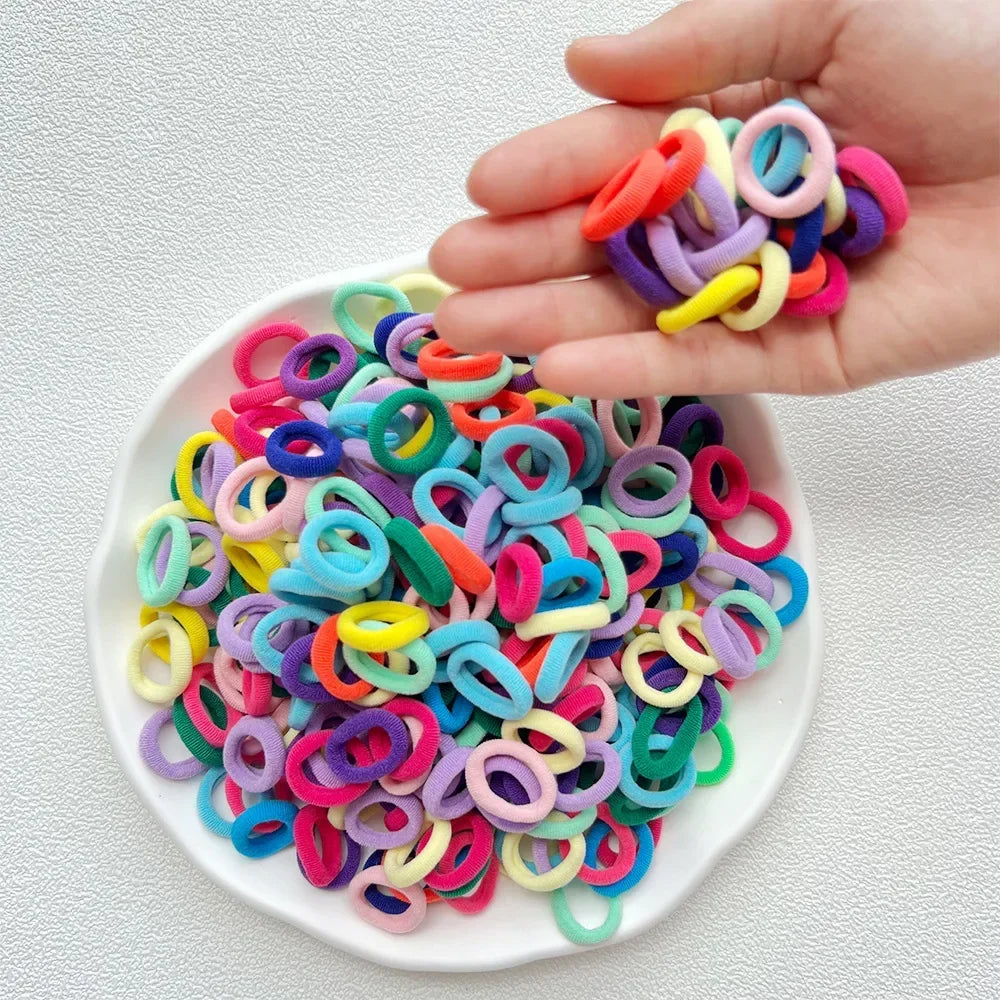 A hand holds a pile of colorful nylon hair ties in various shades of pink, purple, blue, and green.
