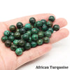 A handful of dark green African Turquoise round beads held in a person's hand.