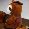 A brown sloth plush toy wearing a brown cap sitting on a wooden surface.