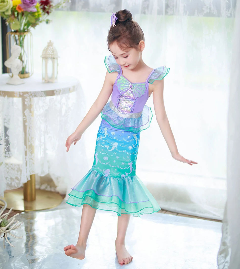 A young girl models a purple and teal mermaid fantasy dress with a ruffled fishtail skirt.