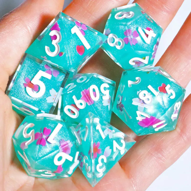 A hand holds a set of teal and pink resin polyhedral dice.
