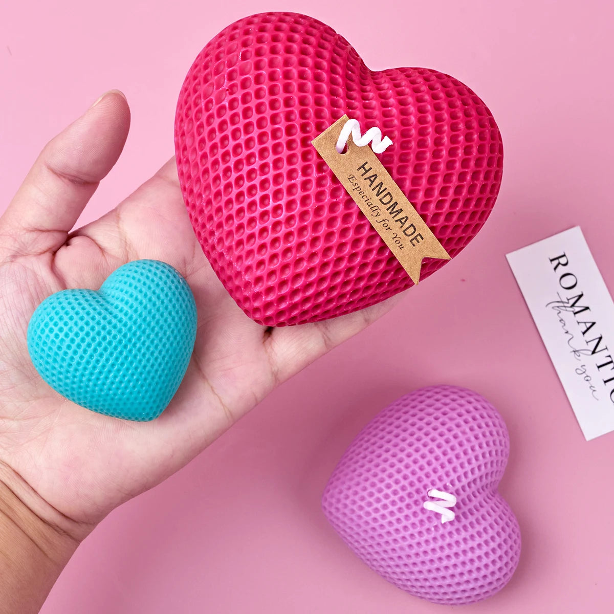 A hand holds a pink textured silicone heart mold, a blue heart, and a purple heart, with a tag labeled Handmade for you.