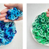 A hand holds a white dish filled with colorful nylon hair ties in shades of blue and green.