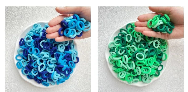 A hand holds a white dish filled with colorful nylon hair ties in shades of blue and green.