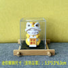 A yellow cat figurine with a white hat is displayed in a clear glass box on a wooden base.