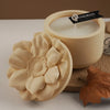 A light yellow floral silicone mold rests next to a candle and a brown leaf on a white surface.