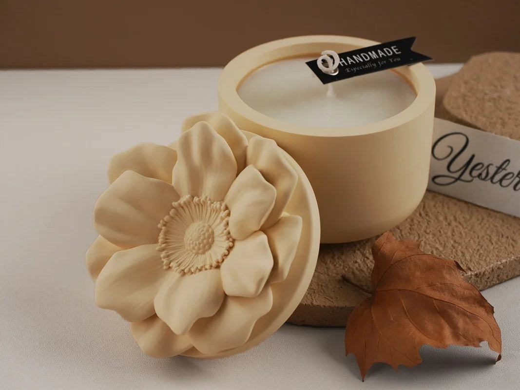 A light yellow floral silicone mold rests next to a candle and a brown leaf on a white surface.