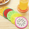 A set of colorful fruit pattern PVC coasters, including slices of orange, watermelon, lime, and kiwi, are displayed on a wood