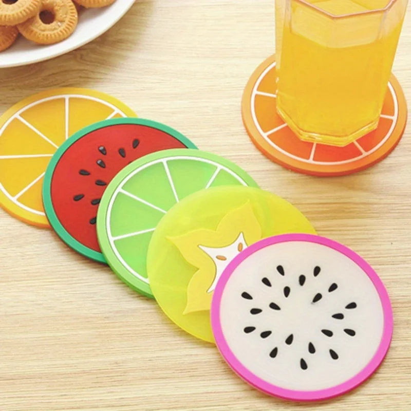 A set of colorful fruit pattern PVC coasters, including slices of orange, watermelon, lime, and kiwi, are displayed on a wood