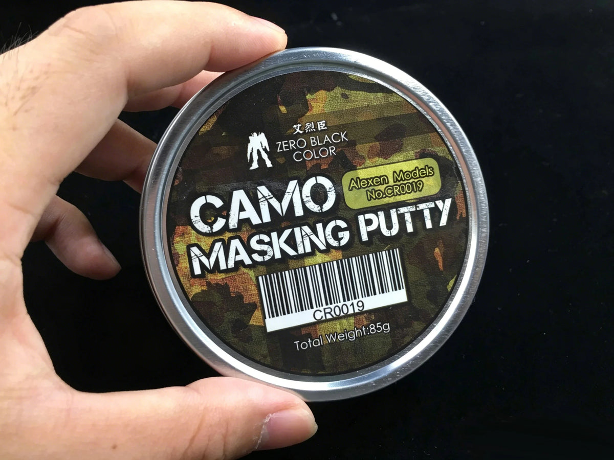 A hand holds a tin of Camo Masking Putty labeled ZERO BLACK COLOR for model painting.