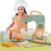 A young girl is playing with a wooden pretend play kitchen set featuring a coffee maker and tea accessories.