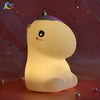 A white unicorn LED night light with a purple horn is illuminated on a pink surface.