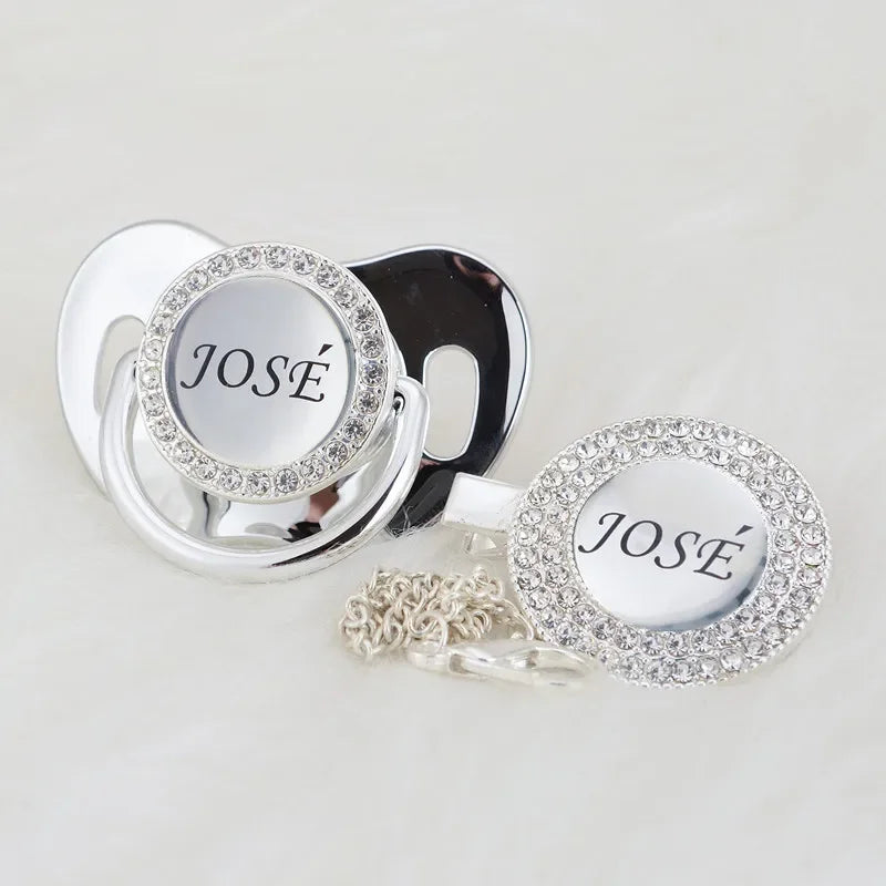 A silver crystal pacifier and clip gift set featuring a circular pendant engraved with the name José