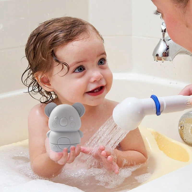 A baby is playing with a soft silicone animal bath toy that sprays water in a bathtub.