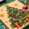 A hand is painting a detailed Christmas tree design using green and red beads on a canvas board.