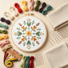 A collection of colorful embroidery threads and a wooden hoop displaying a mandala flower pattern for an embroidery kit.