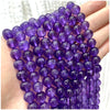 A hand holds a string of purple amethyst and garnet beads for DIY jewelry making.