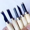A hand holds a set of professional wood carving chisels with black steel blades and light wood handles.