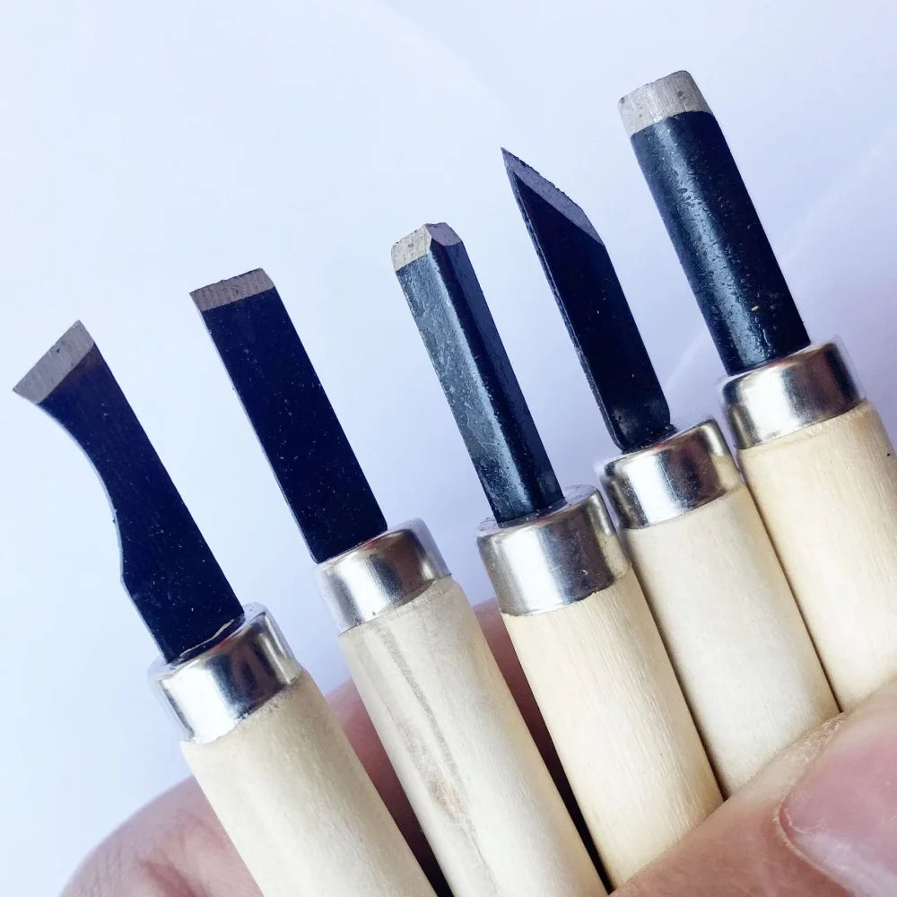 A hand holds a set of professional wood carving chisels with black steel blades and light wood handles.
