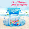 A blue mesh play tent with a bow, filled with colorful plastic balls, set up on a sandy beach.