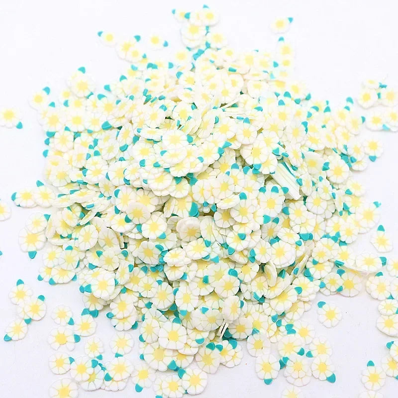 A pile of small polymer clay flower charms in white and light blue colors.