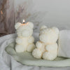 A white silicone mold shaped like a bear is placed on a green surface next to a lit candle.